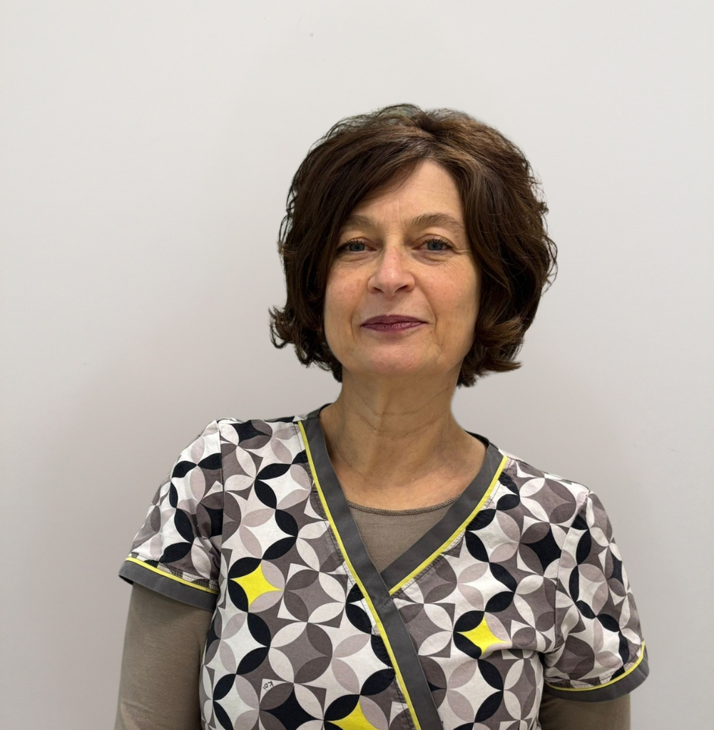 Una donna di mezza età con capelli castani corti e ondulati si staglia su un semplice sfondo bianco. Indossa un camice a fantasia con disegni circolari neri, grigi, bianchi e gialli, che rappresenta il team dedicato del veterinario di Schio, Vicenza.